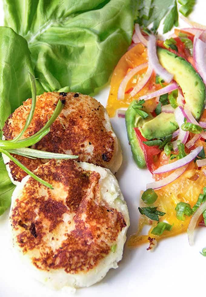 two Ecuadorian cheese and potato patties next to a butter lettuce leaf and a tomato avocado onion salad