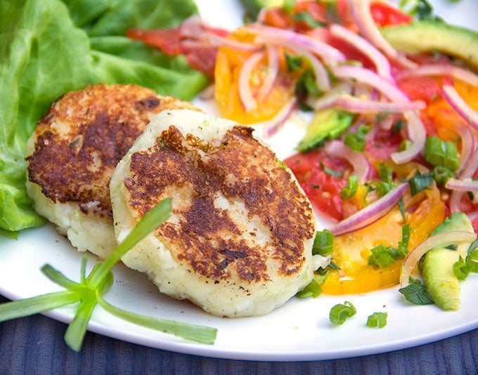 a plate with two potato patties and a tomato avocado red onion salad