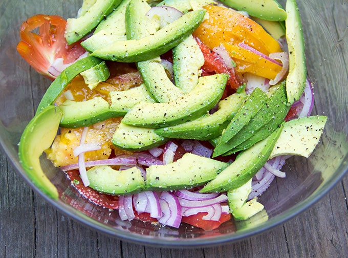 Tomato avocado onion salad in a bowl and sprinkled with salt and fresh cracked pepper