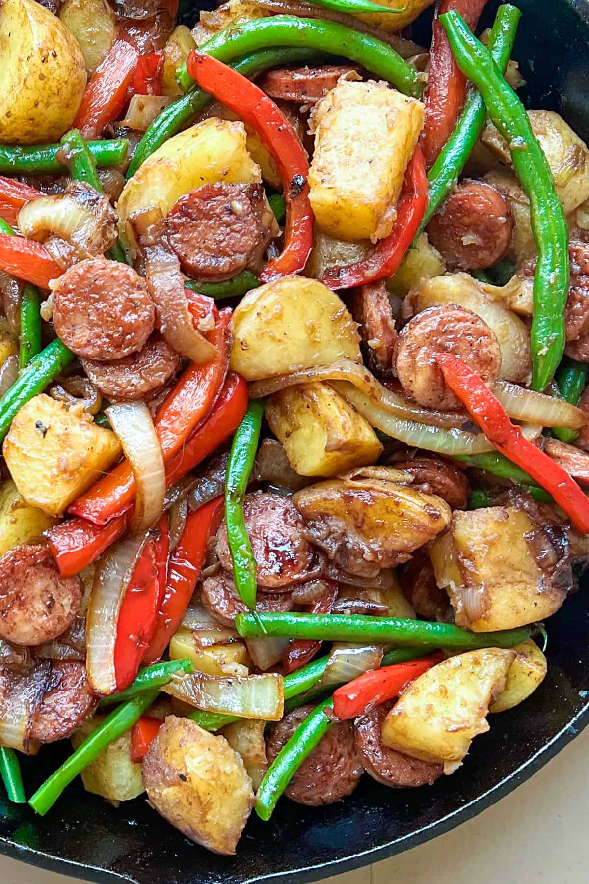 cast iron skillet filled with sautéd slices of sausage, chunks of potato, sliced red bell peppers and green beans