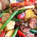 cast iron skillet filled with sautéd slices of sausage, chunks of potato, sliced red bell peppers and green beans