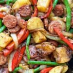 cast iron skillet filled with sautéd slices of sausage, chunks of potato, sliced red bell peppers and green beans