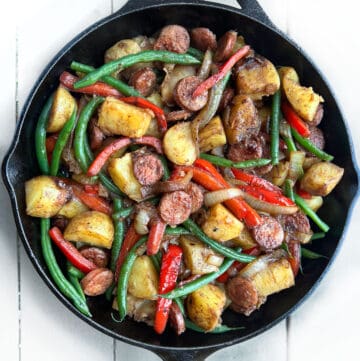 cast iron skillet filled with sautéd slices of sausage, chunks of potato, sliced red bell peppers and green beans