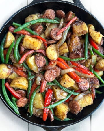 cast iron skillet filled with sautéd slices of sausage, chunks of potato, sliced red bell peppers and green beans