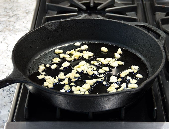 simmering garlic in a cast iron skillet for sautéed spinach with garlic