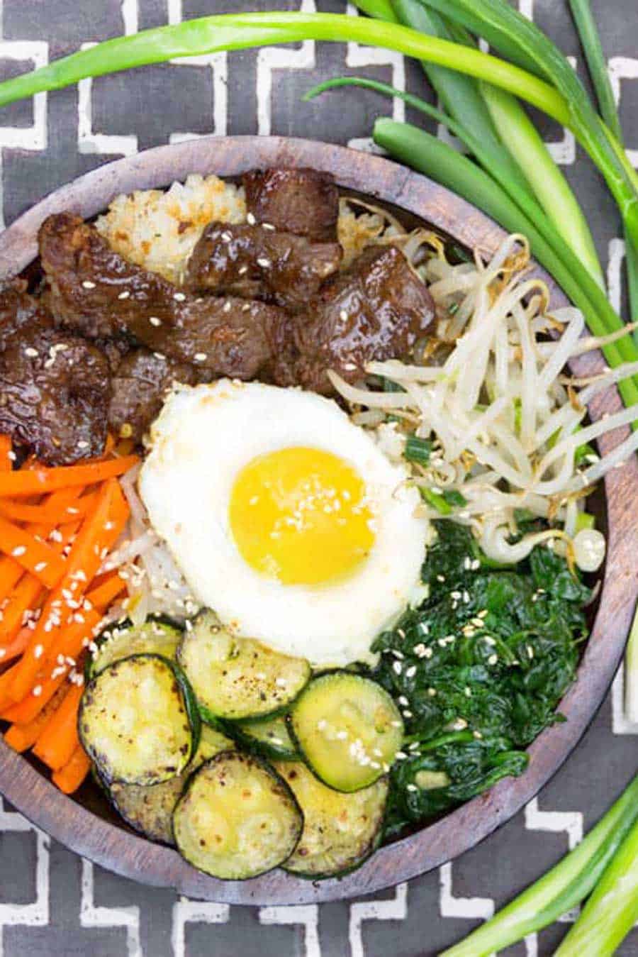 bibimbap bowl with bulgogi beef, carrots sticks, sautéed sliced zucchini, spinach, bean sprouts, and a fried egg in the middle