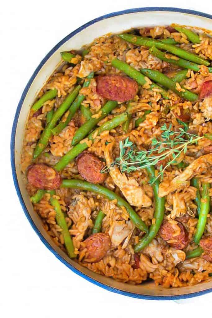 close up looking down into a white pot of spicy chicken jambalaya with sausages and green beans