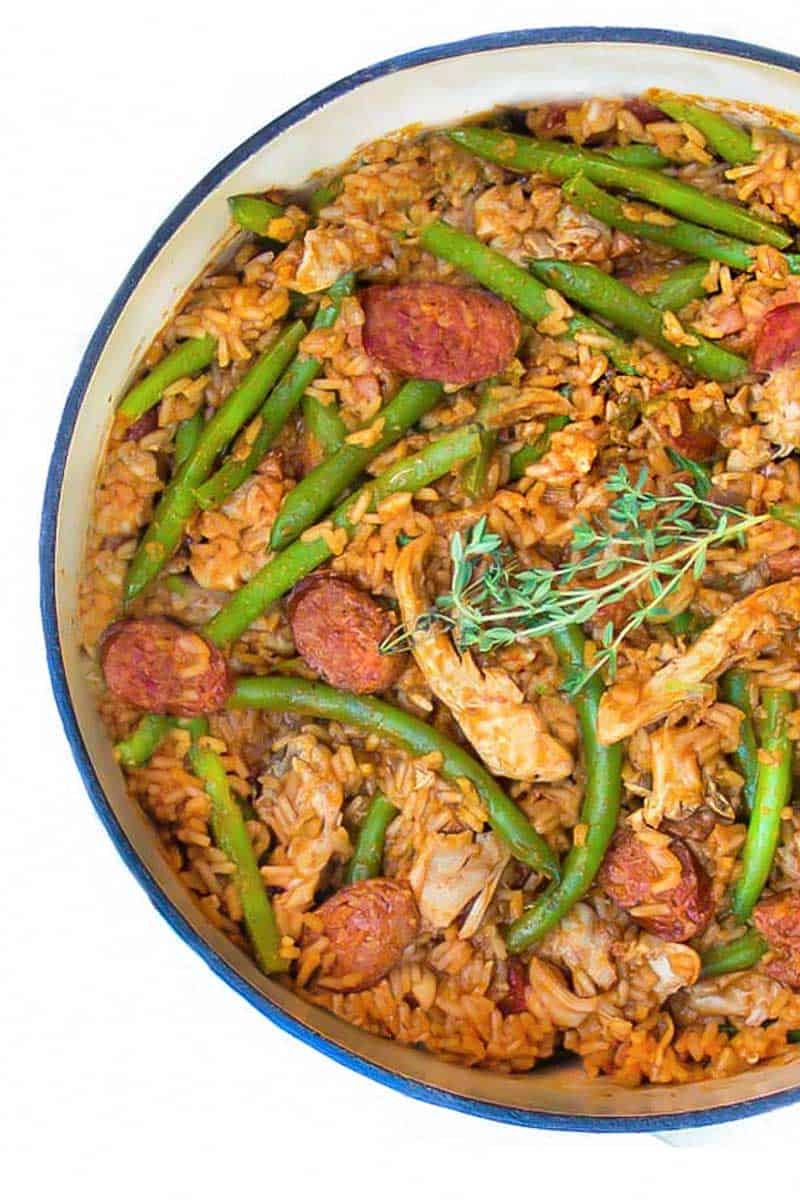 close up looking down into a white pot of spicy chicken jambalaya with sausages and green beans