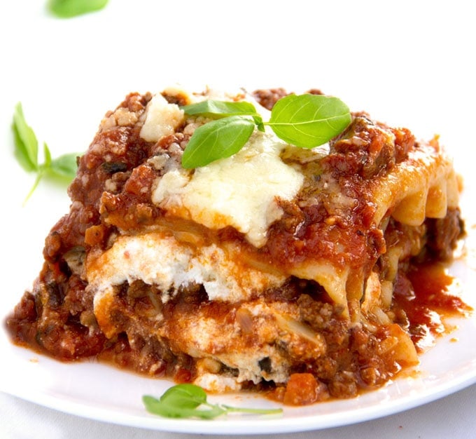 close up of a square of meaty, cheesy, tomatoey lasagna with sprigs of basil on top and scattered around