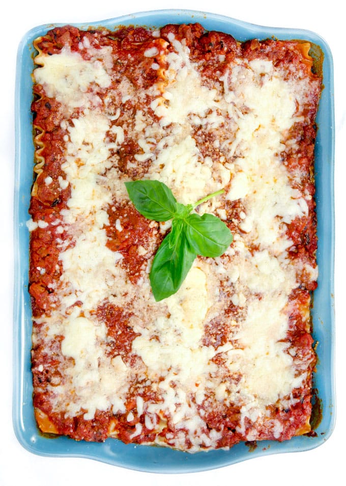 a blue rectangular casserole filled with cheesy lasagna and a sprig of basil in the middle