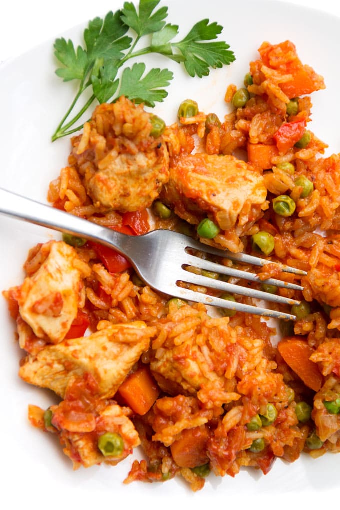 close of of chicken and tomatoey rice on a plate with a fork and sprig of parsley