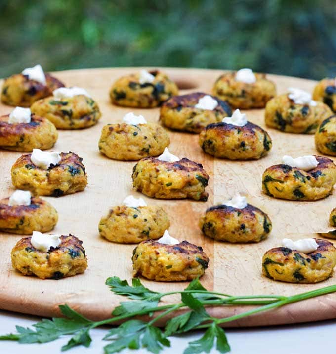 A platter with lots of Mini Spinach and Potato Knishes, topped with sour cream.