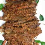 Sliced beef rendang brisket on a white platter with a fork poking in at the top right