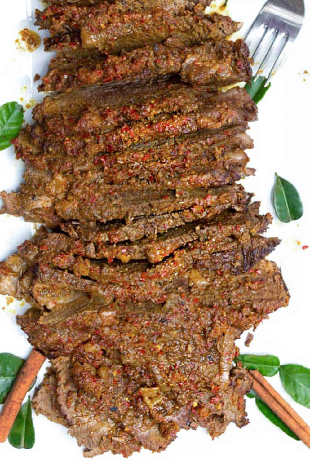 Sliced beef rendang brisket on a white platter with a fork poking in at the top right