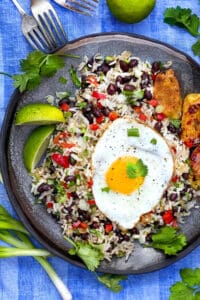 a grey plate on a vivid blue cloth napkin, the plate topped with rice and beans flecked with red bell peppers, scallions and cilantro, and topped with a fried egg