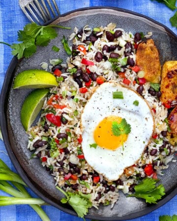 a grey plate on a vivid blue cloth napkin, the plate topped with rice and beans flecked with red bell peppers, scallions and cilantro, and topped with a fried egg