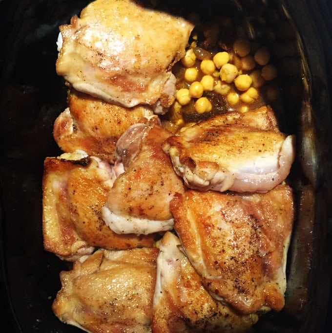 overhead view of inside a crockpot filled with 8 browned chicken thighs, chickpeas and broth