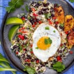 a grey plate on a vivid blue cloth napkin, the plate topped with Costa Rican gallo pinto: rice and beans flecked with red bell peppers, scallions and cilantro, and topped with a fried egg