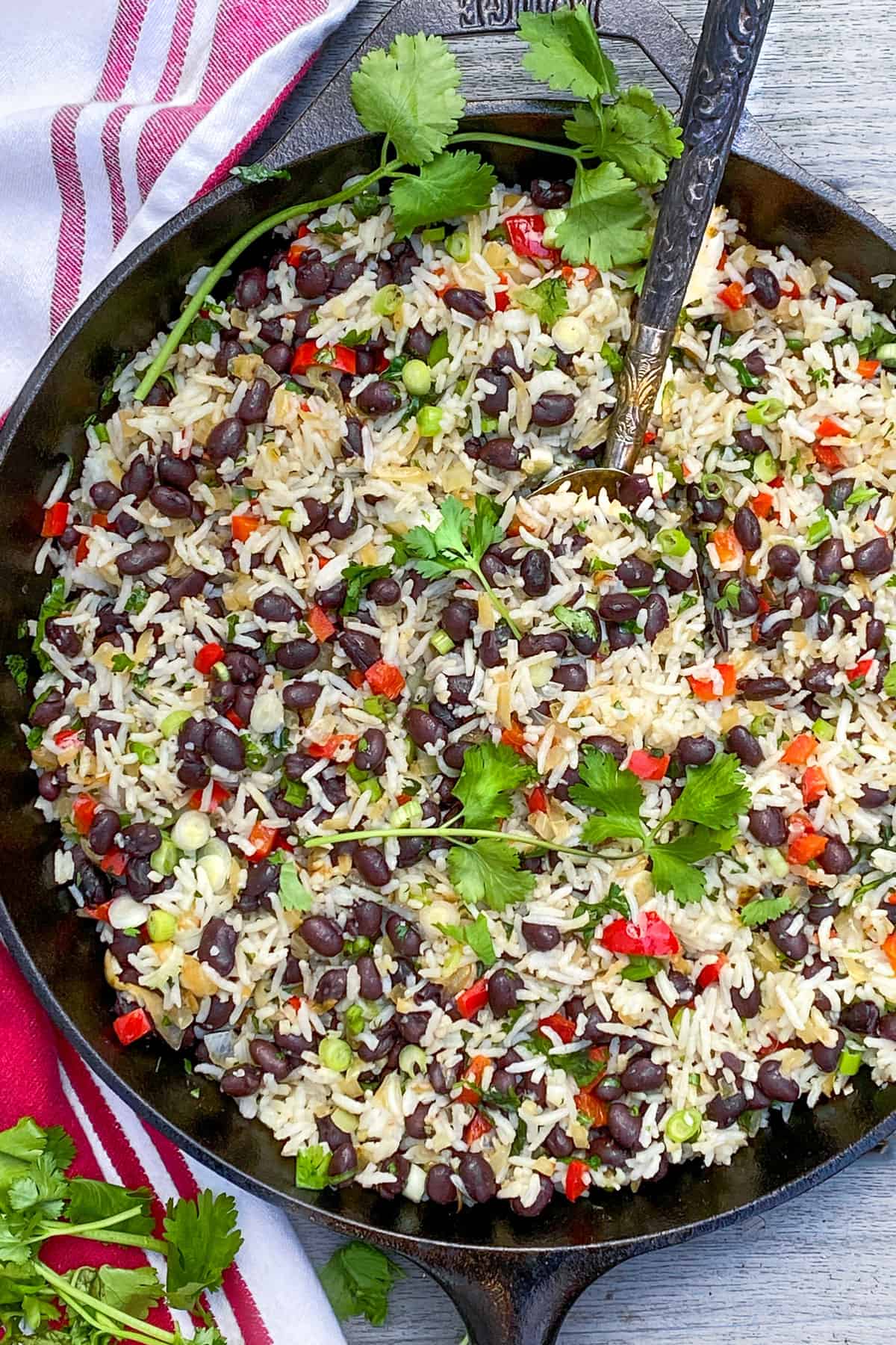 overhead closeup of a cast iron skillet filled with gallo pinto: a rice and beans mixture with bits of chopped red bell pepper, scallions and cilantro