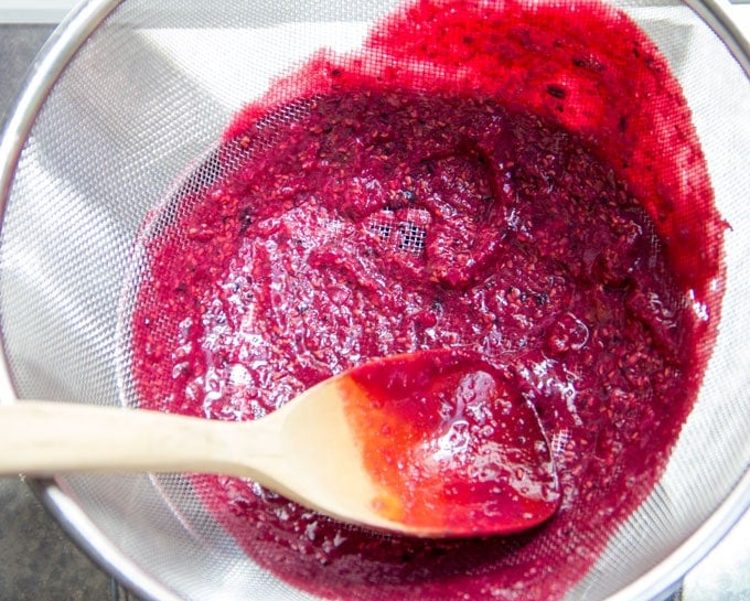 straining berries for berry sauce to serve over pain perdu