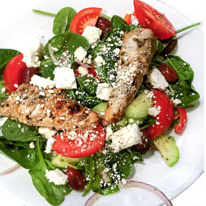 two grilled turkey tips on a bed of spinach with sliced tomatoes, cucumbers, red onion, crumbled feta and kalamata olives.