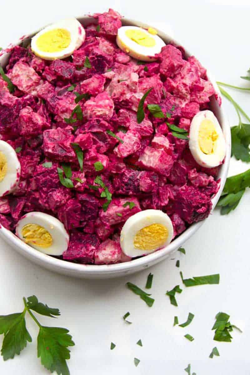 White serving bowl filled with bright pink potato and beet salad, with sliced hard boiled eggs around the edges