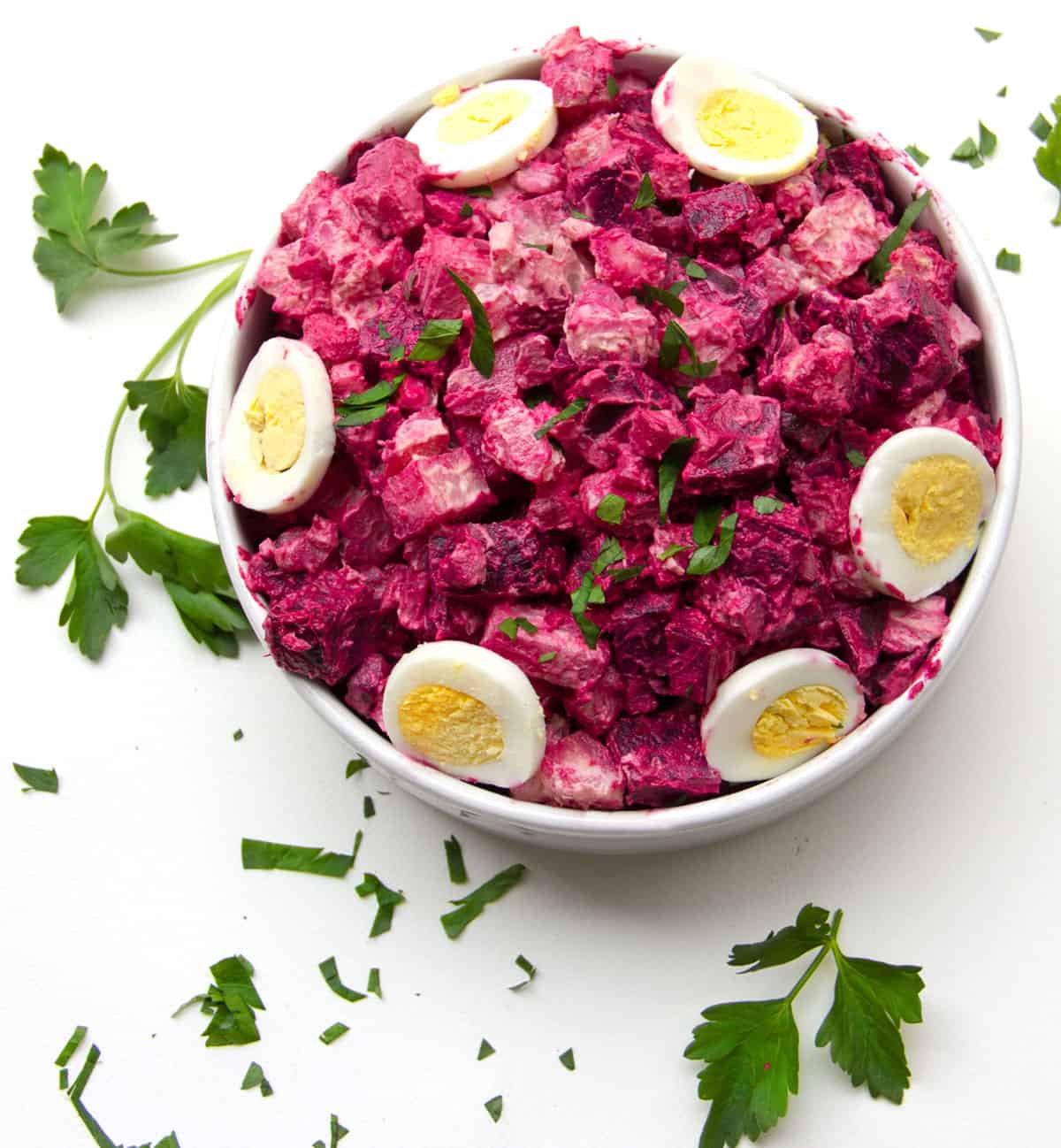 hot pink beet and potato salad in a round serving bowl, topped with sliced hard boiled eggs and chopped parsley