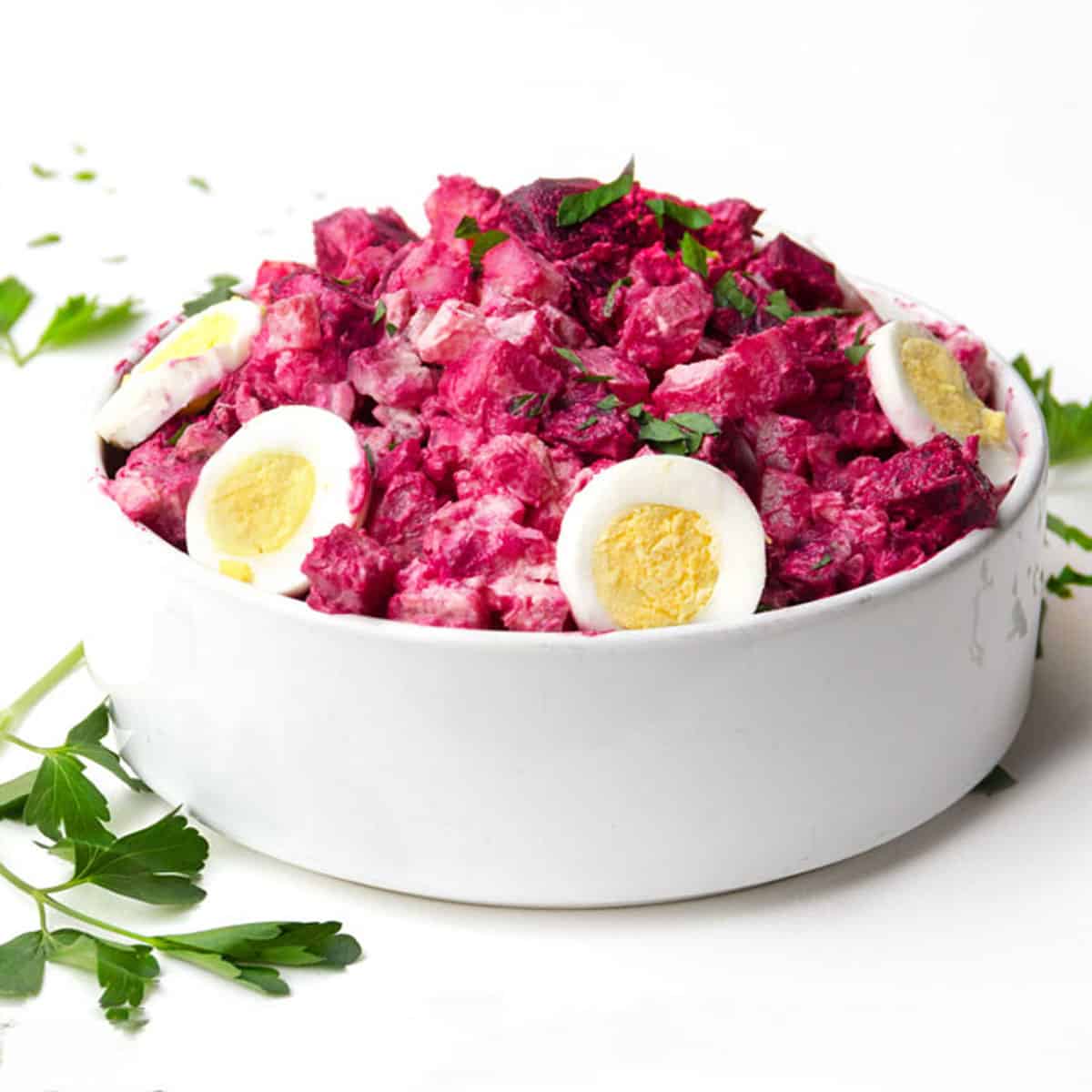 hot pink beet and potato salad in a round serving bowl, topped with sliced hard boiled eggs and chopped parsley
