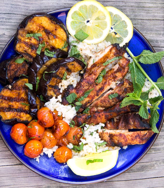 Grilled Harissa Chicken and Eggplant Rice Bowl with cherry tomatoes, lemon slices and a sprig of mint