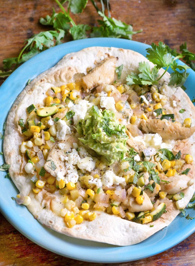 Chicken Tostada: Flour tortilla topped with chicken, corn, zucchini, feta and avocado salsa