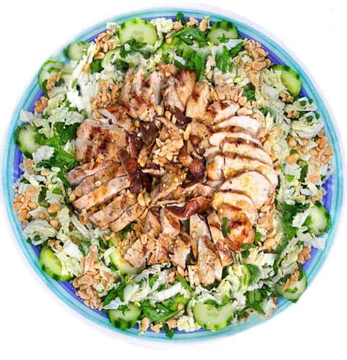 Round platter topped with shredded cabbage and cucumber salad topped with sliced grilled chicken and shiitake mushrooms.