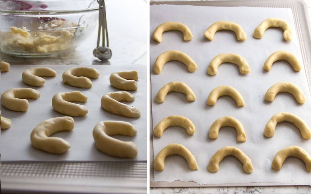 A parchment-lined cookie sheet topped with 15 pieces of crescent-shaped cookie dough, ready to go into the oven to bake