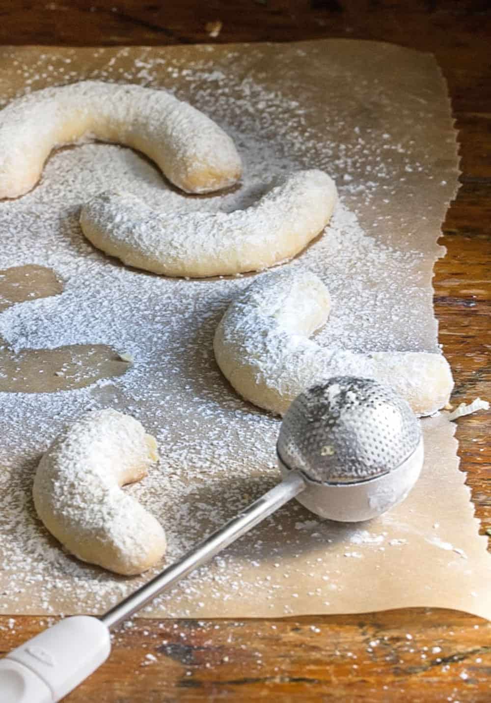 close up of 4 sugar dusted almond crescent cookies with a metal sugar dusting tool