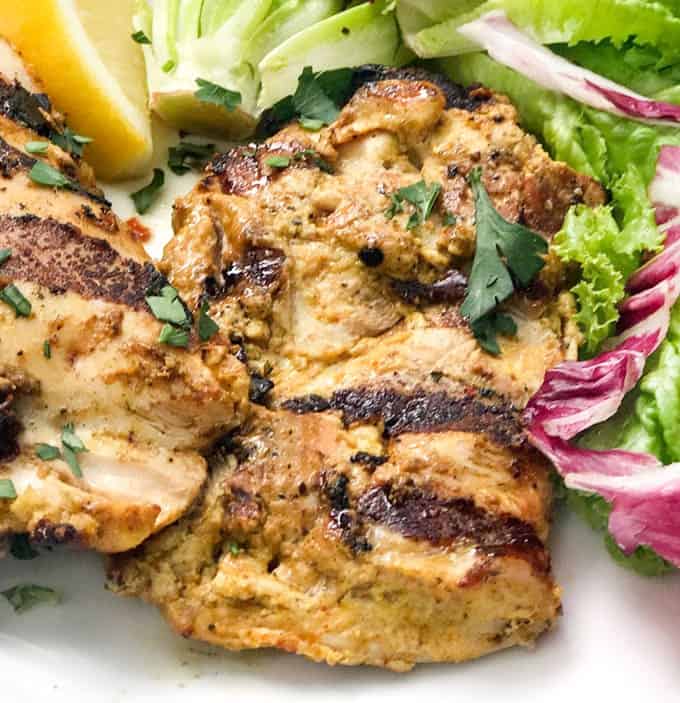 two boneless grilled chicken thighs on a plate with salad.