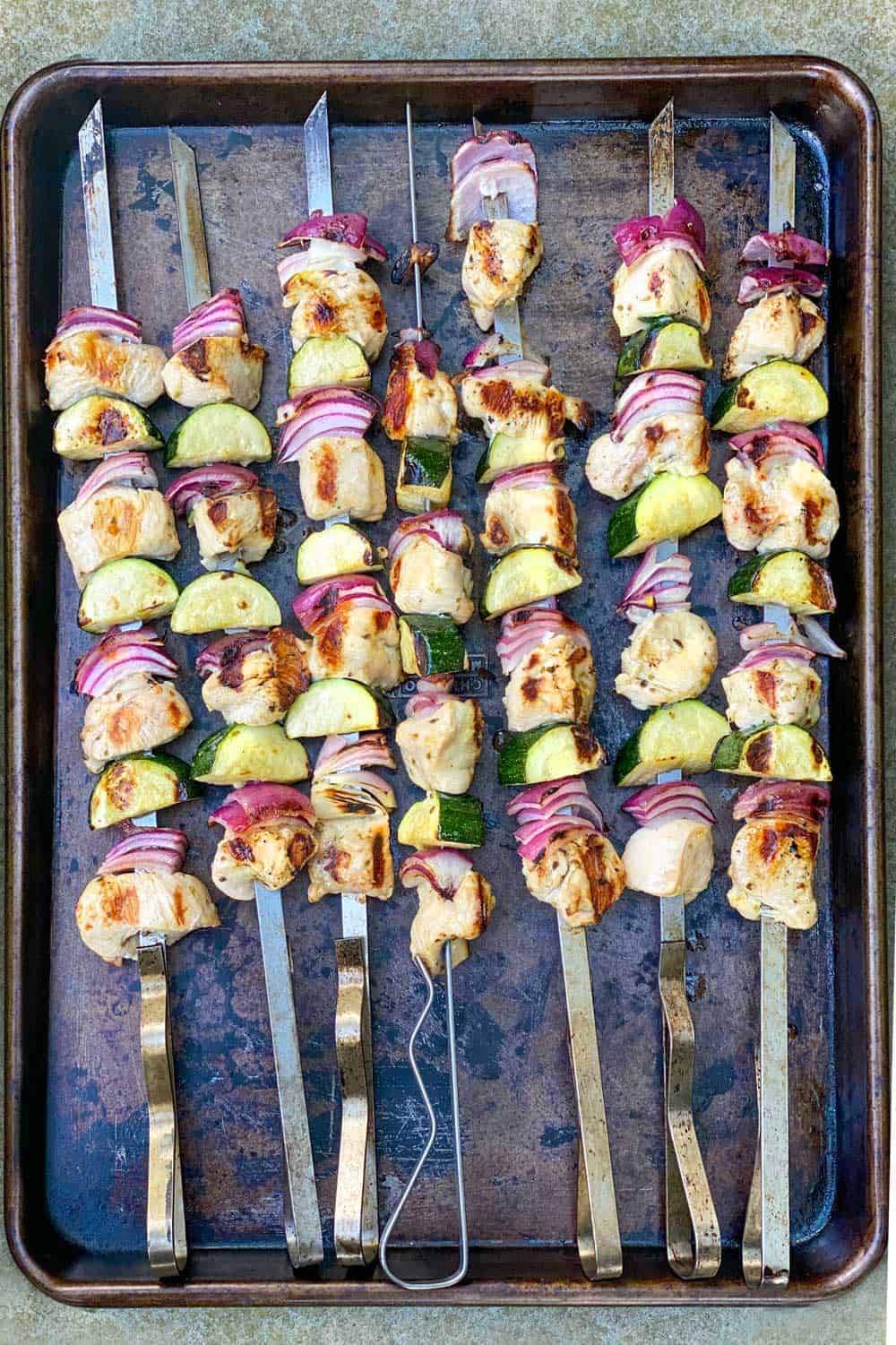 7 skewers of grilled chicken souvlaki with zucchini and red onions.