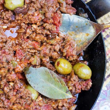 cuban picadillo in a black skillet with green olives and a bay leaf