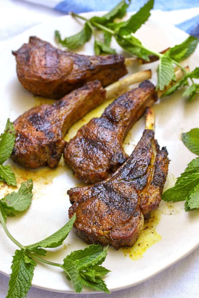 4 grilled spiced baby lamb chops on a platter with sprigs of cilantro.