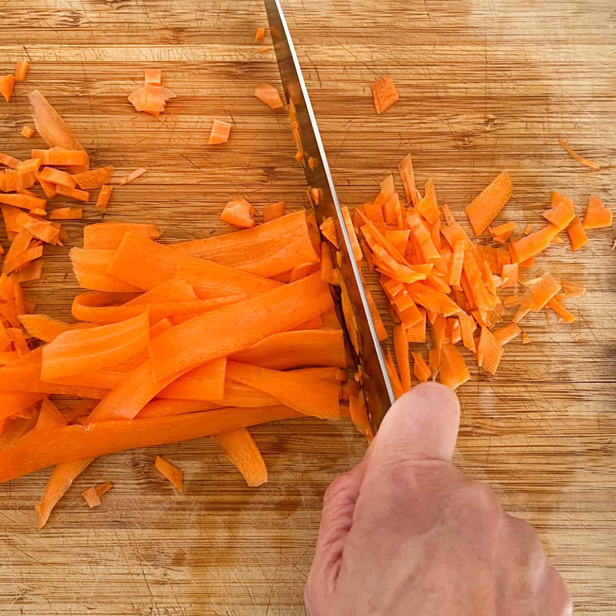 Wide thin strips of carrot clustered together and getting sliced thinly crosswise into finely chopped carrot pieces.
