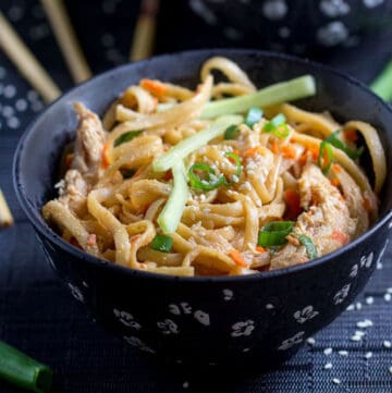 bowl filled with sesame coated linguine noodles, topped with matchstick cucumbers and carrots, sliced scallions and sesame seeds.