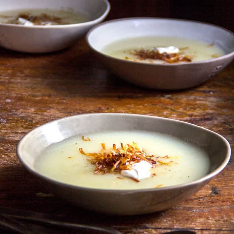 Two bowls of potato leek soup topped with a dollop of sour cream and a small pile of frizzled leeks in the center.