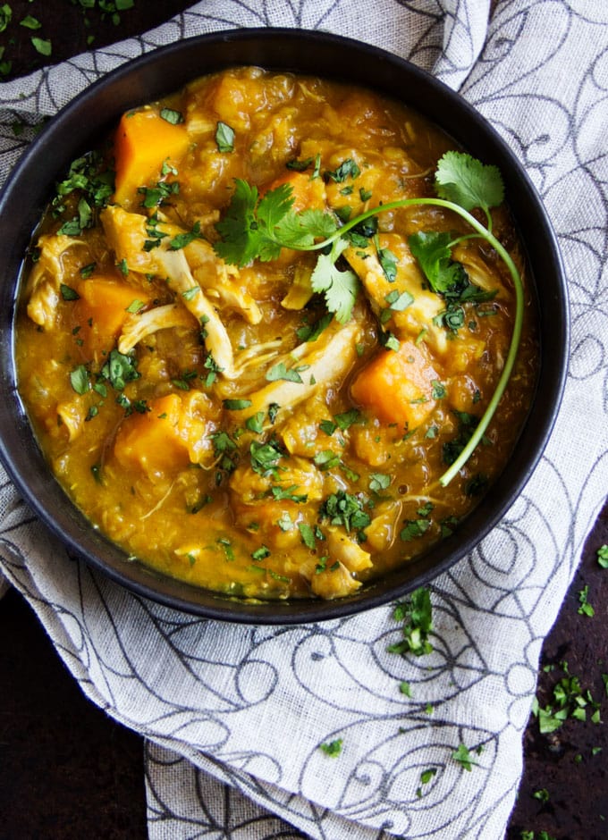 Bowl of curried butternut squash, lentil, and chicken stew with a sprig of cilantro.