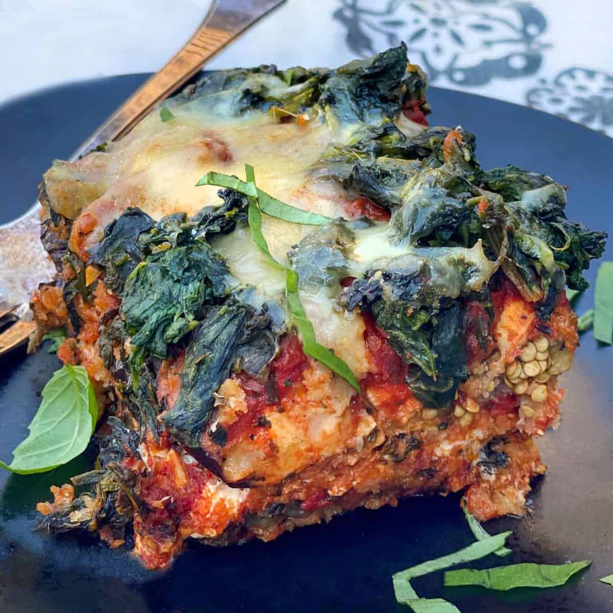 square piece of eggplant parmesan topped with spinach and cheese on a black plate