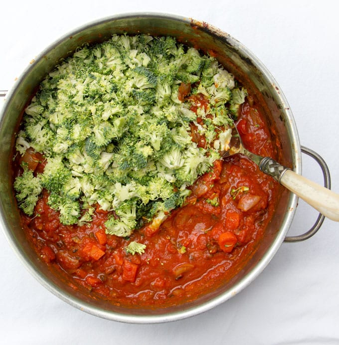 overhead shot of a sauce pot filled with sauce and half of it is covered with shaved broccoli 