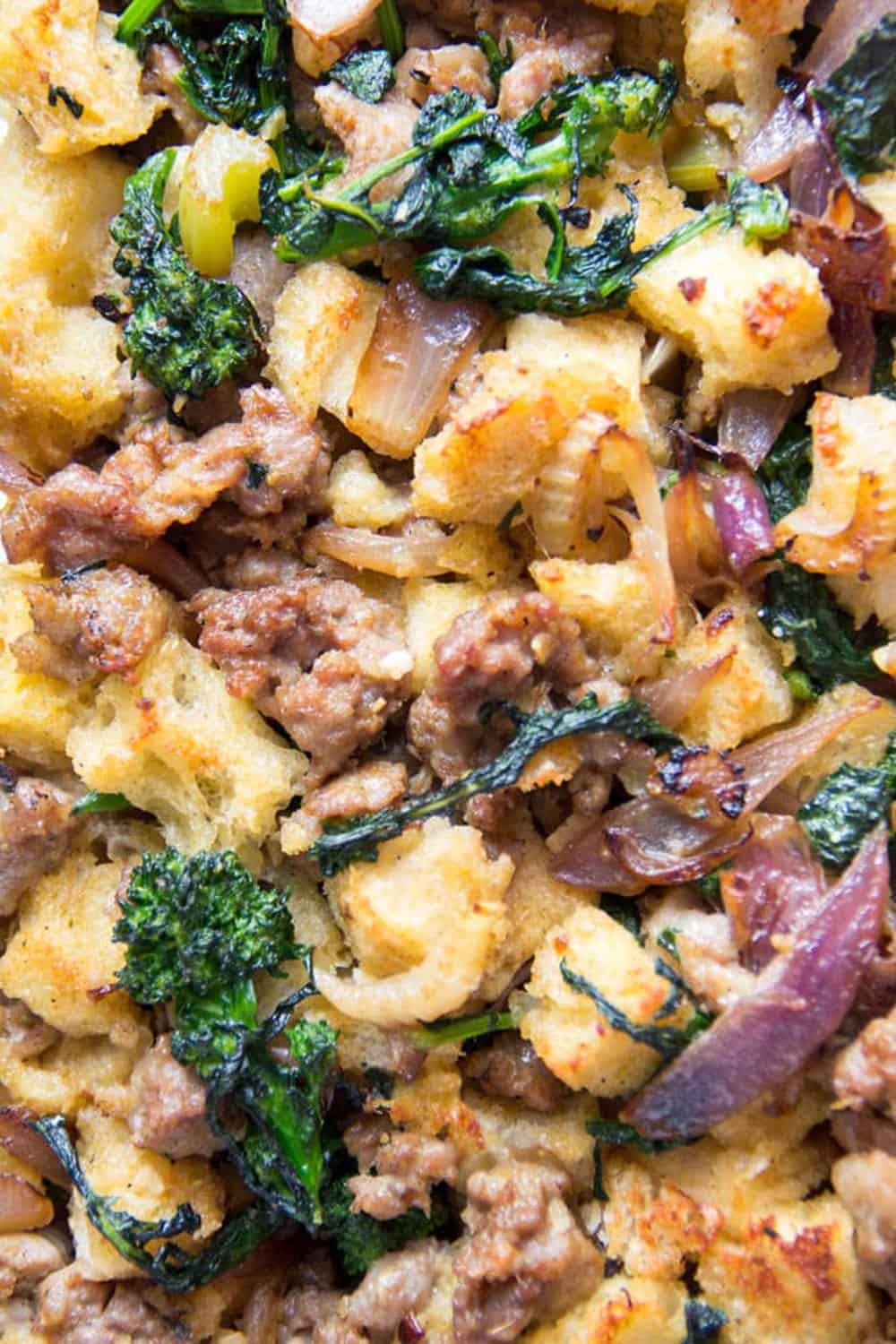 close up of Thanksgiving stuffing with bread cubes, big pieces of sausage, broccoli rabe and red onions