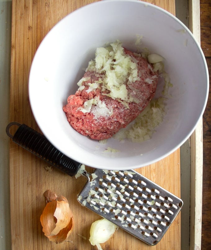 white bowl filled with raw ground beef, grated onions and salt.