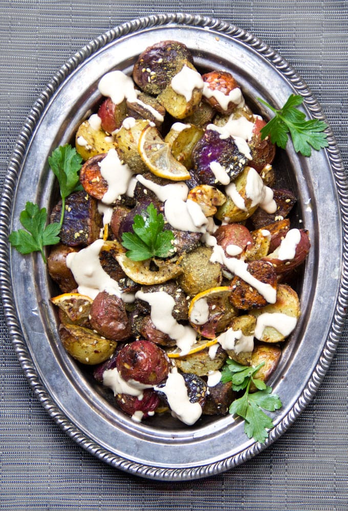 rainbow roasted potatoes on a silver platter drizzled with tahini and garnished with parsley