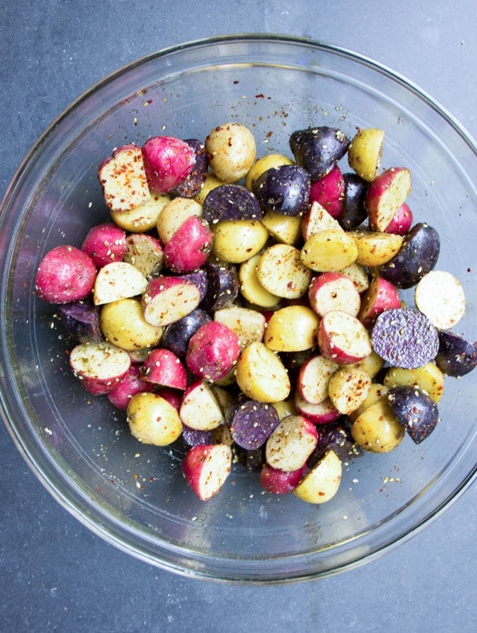 A glass bowl with rainbow colored raw Potatoes sliced in half and tossed with oil and Za'atar 