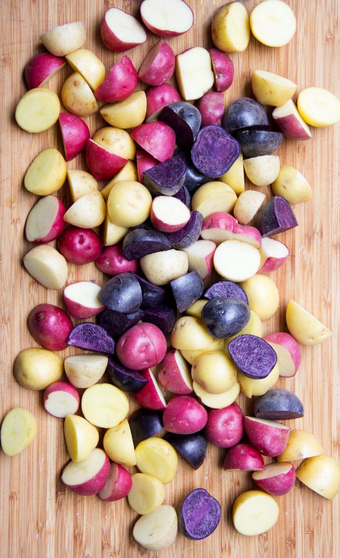 a wooden cutting board with purple, pink, and yellow potatoes, sliced in half.