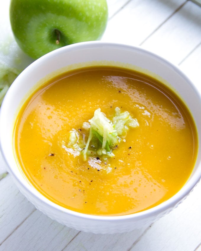 close up of a bowl of curried butternut squash soup, garnished with shredded apples and black pepper.