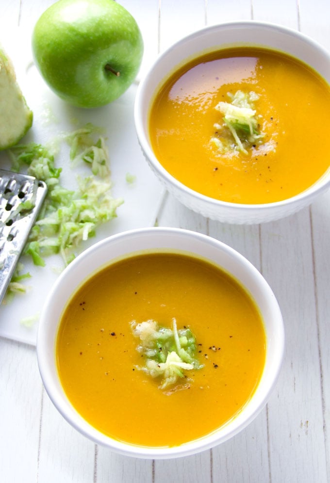 two bowls of curried butternut squash soup topped with shredded granny smith apples